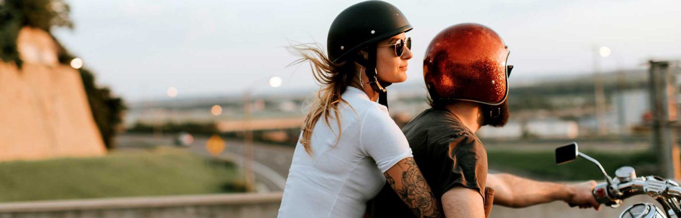 VALYOU Impressum Eine Frau und ein Mann, beide mit Motorradhelm, fahren auf einem Motorrad.